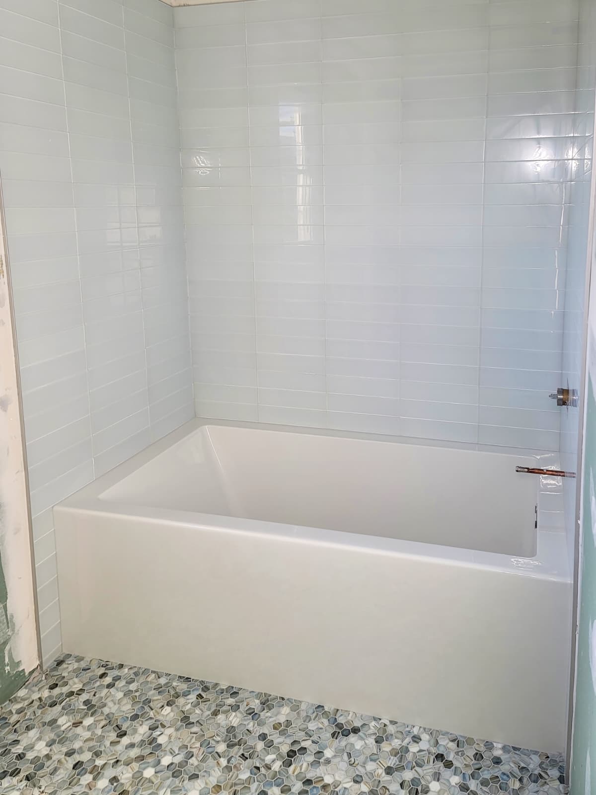 White tile tub surround with pebble mosaic bathroom floor