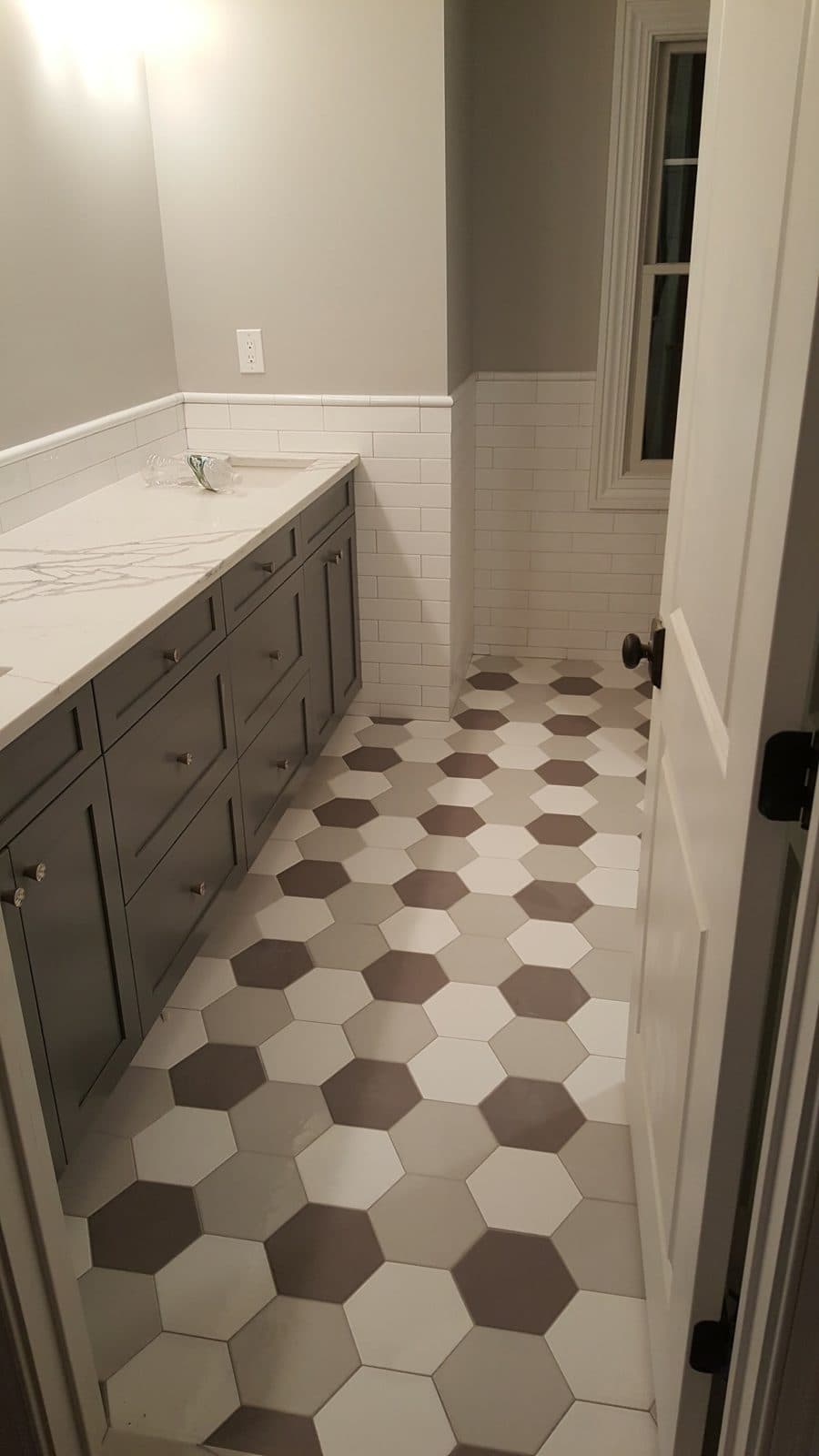 Bathroom floor in white, gray and brown hexagon tile with wainscot walls