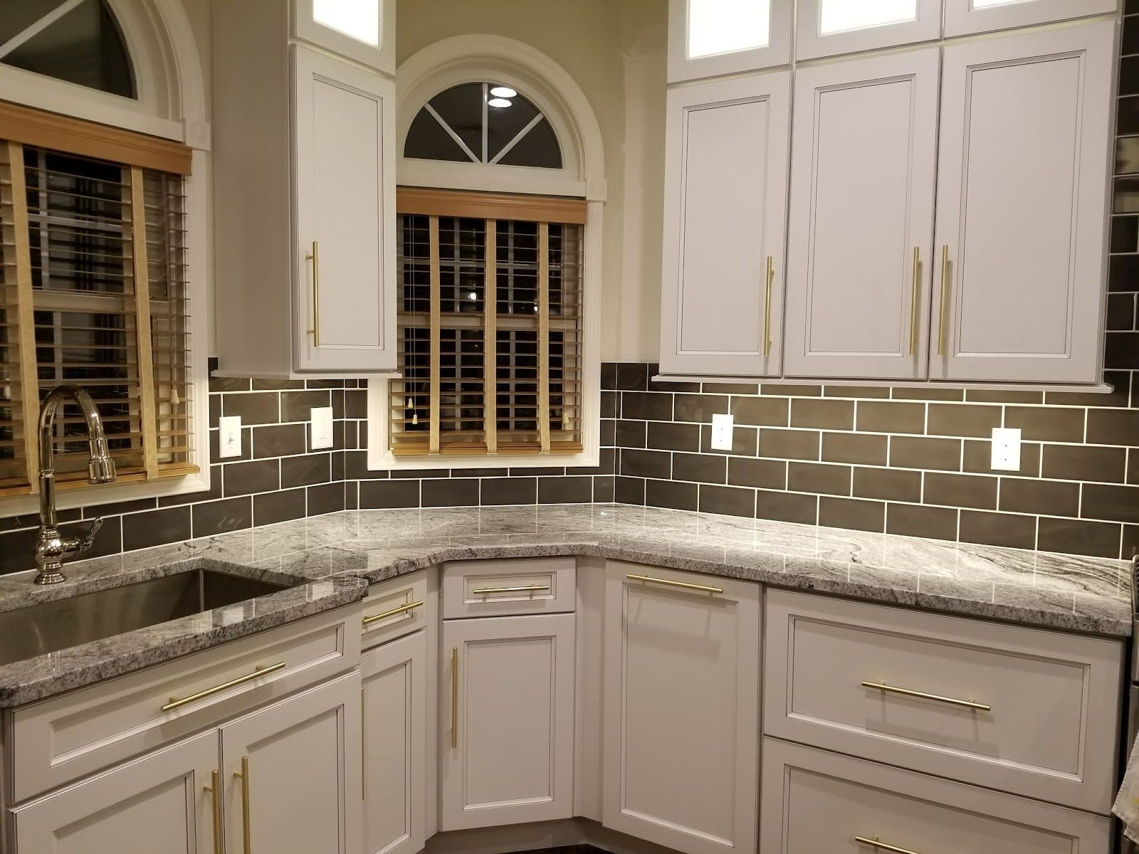 Kitchen backsplash in gray-green subway tile around white cabinets and a corner sink